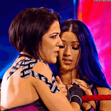 two female wrestlers are hugging each other and one of them is wearing a black and white tape that says backtape on it