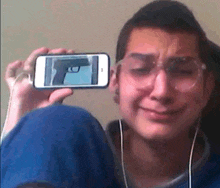 a man is crying while holding up a cell phone with a picture of a gun on it