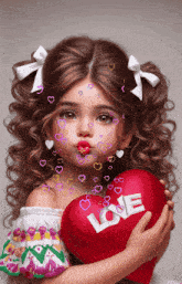 a little girl is blowing a kiss while holding a heart that says love
