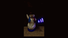 a snowman with a blue scarf and a black hat is dancing in the dark