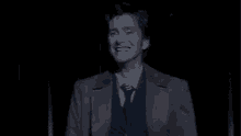 a man in a suit and tie is standing in the dark and smiling .