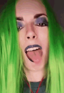 a close up of a woman with green hair sticking her tongue out .