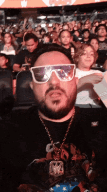 a man wearing sunglasses and a necklace with the letter w on it sits in a crowd