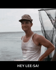 a man wearing a hat and a tank top stands in front of a body of water with the words hey lee-sa below him