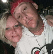 a man and a woman are posing for a picture . the man is wearing a red bandana .