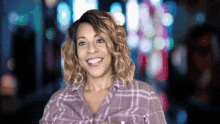 a woman in a purple plaid shirt is smiling in front of a blurry background