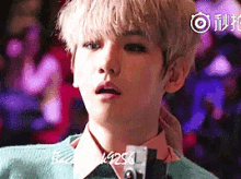 a young man with blonde hair is wearing a green sweater and a pink shirt and tie .