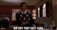 a man in a plaid sweater and tie is standing in a living room .