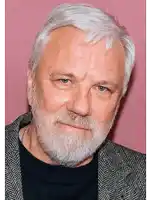 a man with gray hair and a beard is wearing a black shirt and a grey jacket