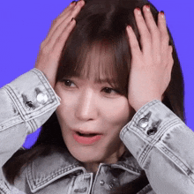 a woman in a denim jacket is holding her head with both hands