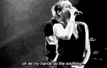 a black and white photo of a man singing into a microphone with the words `` oh let my hands do the soothing '' .