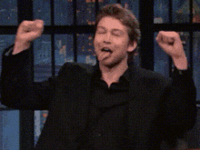 a man in a black suit and black shirt is raising his arms in the air