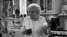 an elderly woman is standing in a kitchen holding a cup of coffee and a candle .