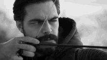 a man with a beard is holding a bow and arrow in a black and white photo .