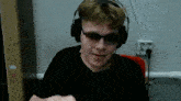 a young man wearing headphones and sunglasses is sitting in front of a wall .