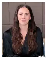 a woman with long brown hair is wearing a black shirt and making a face .