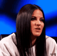 a woman with long black hair is sitting in a chair with a blue background .