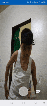 a boy in a white tank top is standing in front of a door with the time 7:26 pm