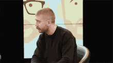 a man with a beard and mustache is sitting in a chair in front of a cartoon face .