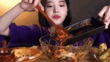 a woman is eating a bowl of food with a wooden spoon and a pan .