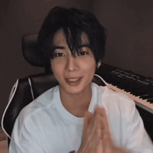 a young man in a white shirt is sitting in a chair in front of a keyboard