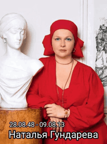 a woman in a red dress is standing next to a white bust