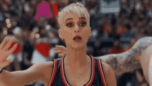 a woman in a basketball uniform is standing in front of a crowd and making a funny face .