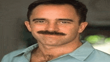 the man is wearing a blue shirt and has a mustache .