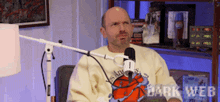 a bald man is sitting in front of a microphone wearing a sweater that says ' dark web ' on it