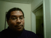 a man wearing glasses and a purple shirt is standing in a hallway