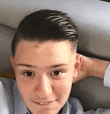 a young boy is laying on a couch taking a selfie with his hand behind his head .