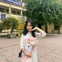 a girl holds a bouquet of flowers in front of a building with a sign that says " thay co "