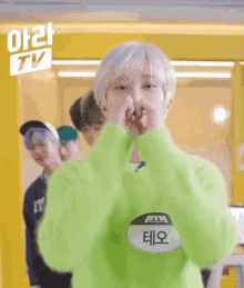 a person wearing a neon green sweater making a heart shape