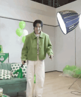 a man in a green jacket stands in front of a green couch with polka dot pillows
