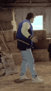 a man in a blue jacket and white sleeves is dancing in front of hay bales