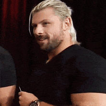 a man with blonde hair and a beard wearing a black shirt and a watch