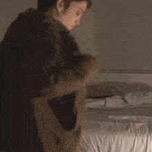 a man is standing in front of a bed wearing a black jacket .