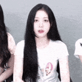 a girl with long black hair is wearing a white t-shirt with a pink circle on it