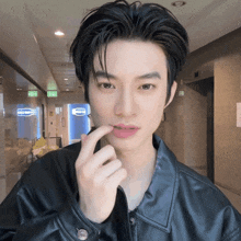 a man wearing a black leather jacket holds his finger to his mouth