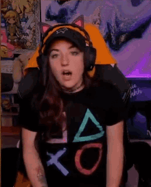 a woman wearing headphones and a playstation t-shirt is sitting in a gaming chair .