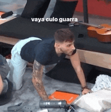 a man is kneeling down on the floor next to a guitar .
