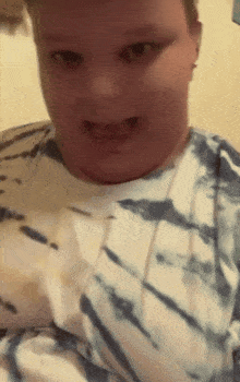 a boy wearing a tie dye shirt is making a face