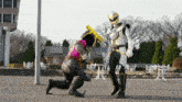 a man in a white and gold costume is kneeling down next to a man in a pink and black costume