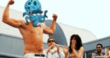 a shirtless man with an octopus on his head stands in front of a crowd