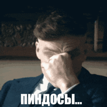 a man in a suit and tie covering his face with his hand with a caption that says pindos