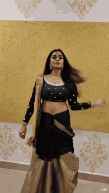 a woman in a black and gold saree is dancing