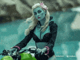 a woman with blue paint on her face is riding a motorcycle