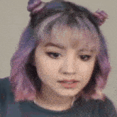 a woman with purple hair and two buns on her head is looking at the camera .