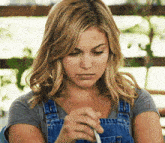 a woman wearing overalls and a grey shirt is looking down