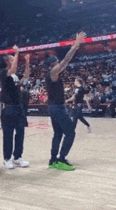 a man in a black tank top is dancing on a basketball court in front of a crowd .